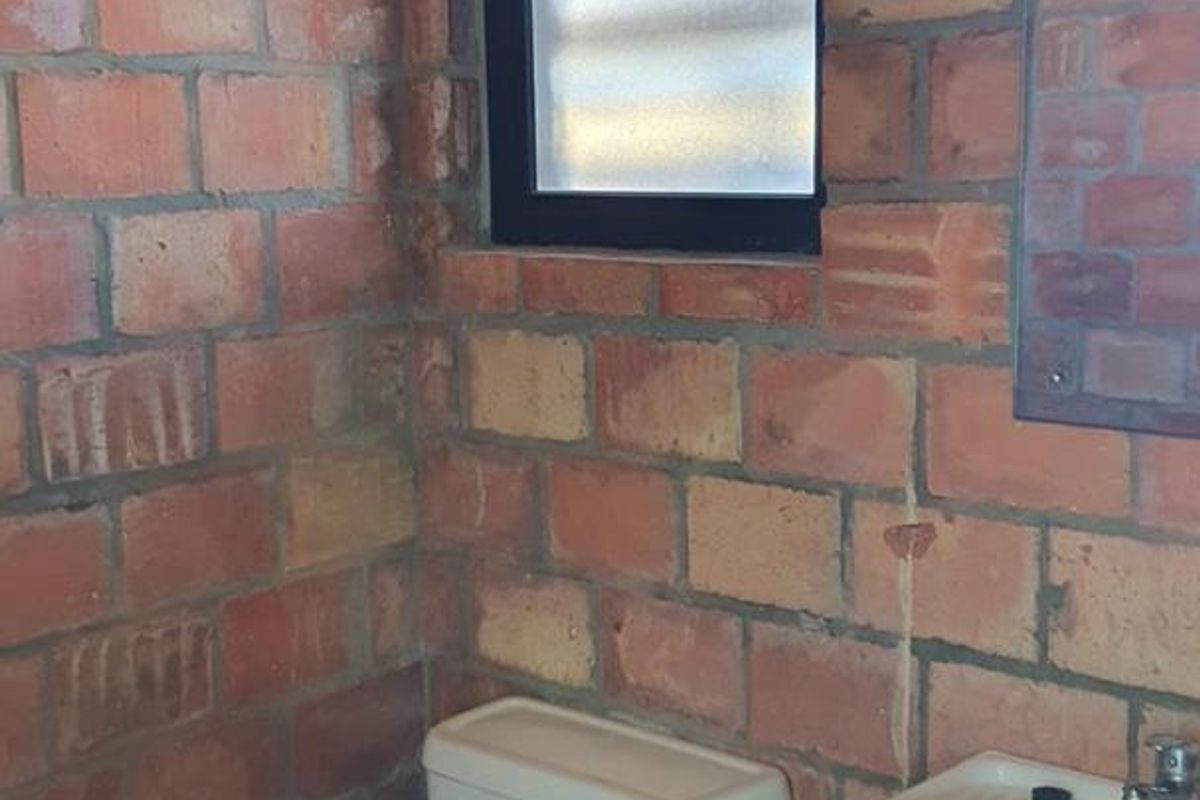A compact bathroom featuring exposed brick walls, a standard toilet, and a wall-mounted washbasin with visible plumbing.