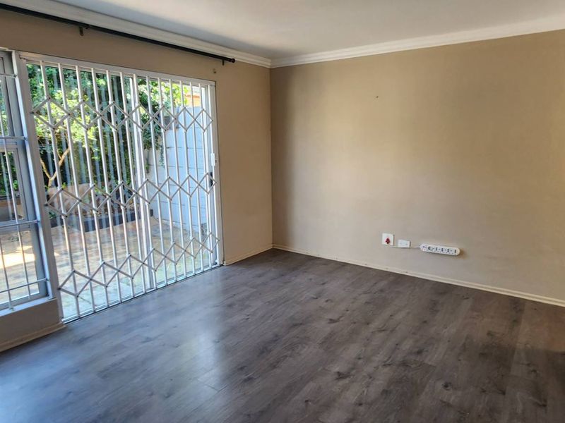 An empty living area featuring laminate flooring, a sliding door with a security gate, and neutral wall finishes.