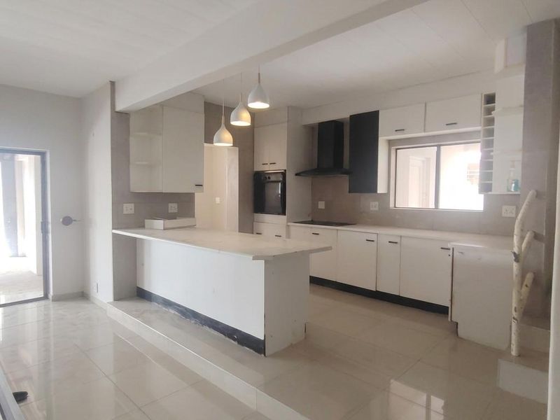 Modern open-plan kitchen featuring white cabinetry, stone countertops, built-in oven, extractor fan, and tiled flooring, with a raised island breakfast bar.