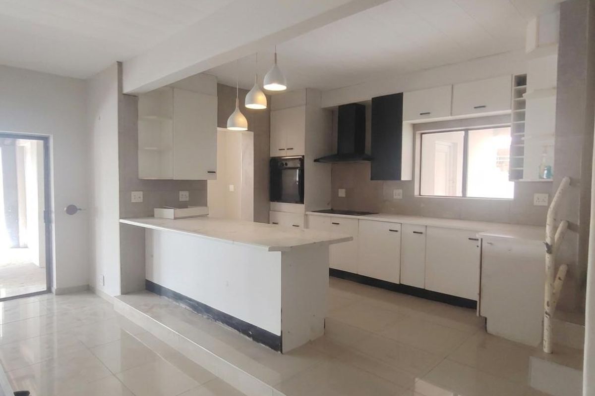 Modern open-plan kitchen featuring white cabinetry, stone countertops, built-in oven, extractor fan, and tiled flooring, with a raised island breakfast bar.