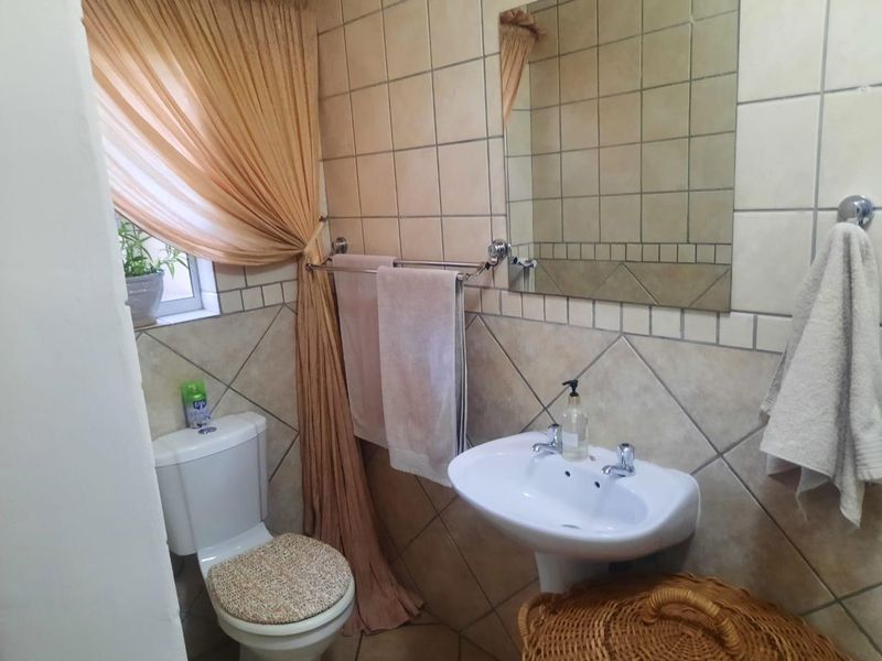 A functional bathroom featuring a pedestal basin, ceramic toilet, and neutral wall tiling with a wall-mounted mirror.