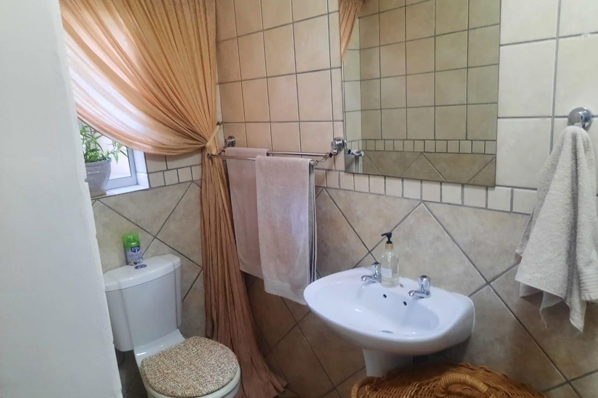 A functional bathroom featuring a pedestal basin, ceramic toilet, and neutral wall tiling with a wall-mounted mirror.