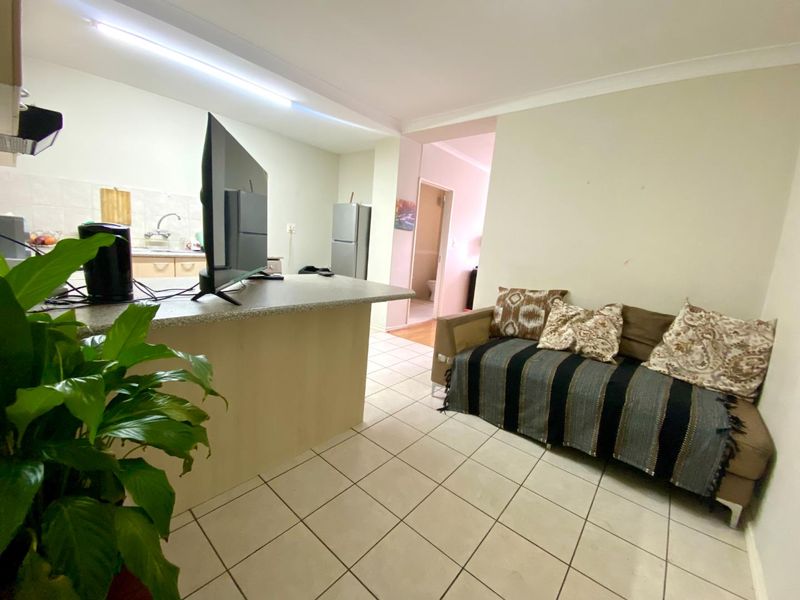 Open plan living area featuring a kitchen with breakfast bar and tiled flooring, leading through to an adjacent room.