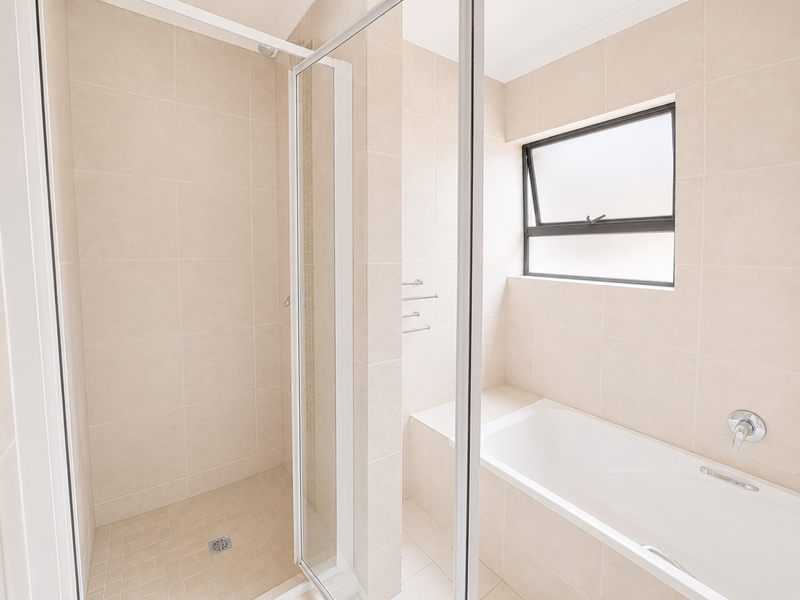 A clean, modern bathroom featuring a separate shower enclosure, a built-in bathtub, and neutral floor-to-ceiling tiling with an awning window for natural light.