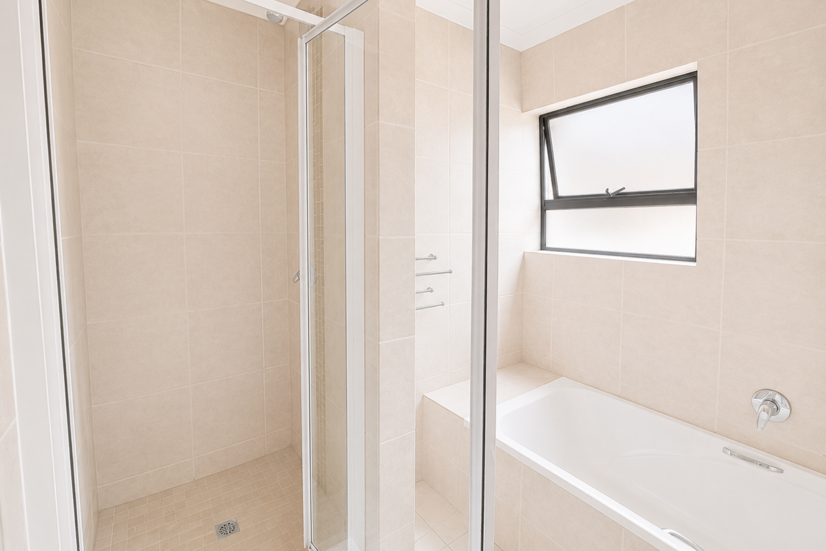 A clean, modern bathroom featuring a separate shower enclosure, a built-in bathtub, and neutral floor-to-ceiling tiling with an awning window for natural light.