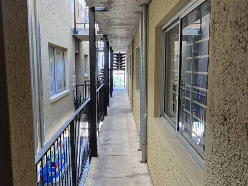 An exterior apartment access walkway featuring a concrete floor, metal balustrade, and sliding windows with security bars.
