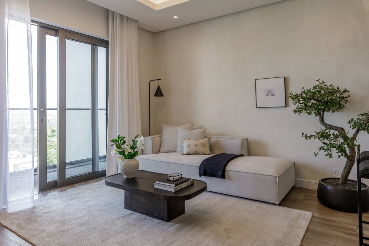 A bright and modern living area featuring neutral tones, recessed ceiling lighting, and large sliding glass doors leading to a private balcony.