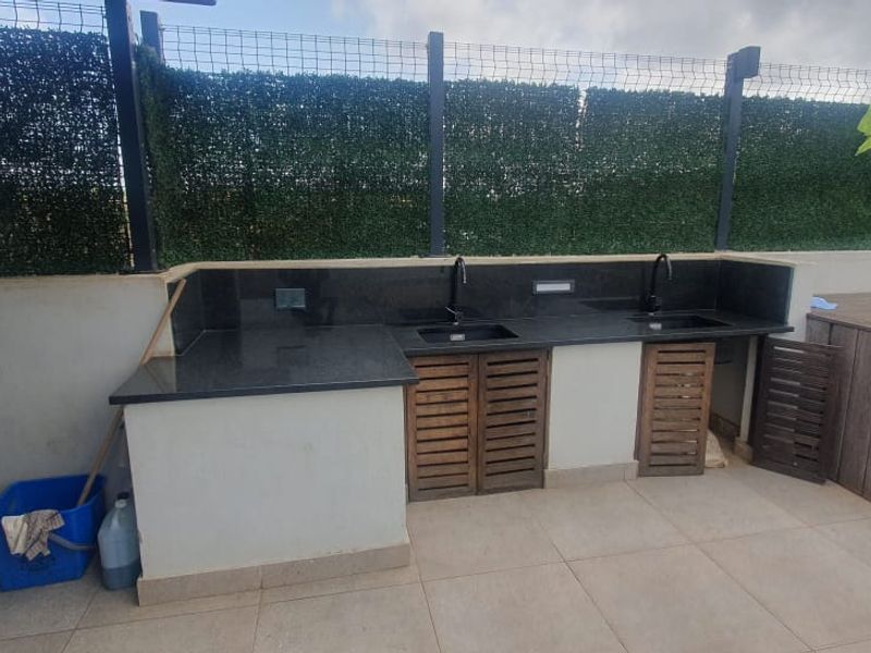 Outdoor patio area featuring a built-in kitchen with granite countertops, dual sinks, and timber decking, enclosed by privacy screening.
