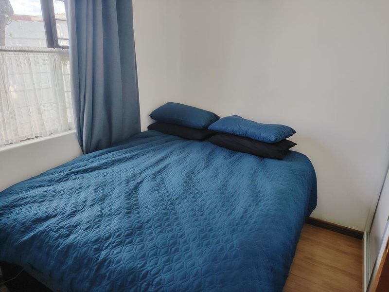 A compact bedroom featuring laminate flooring and a window with curtains, providing a functional and neutral space.