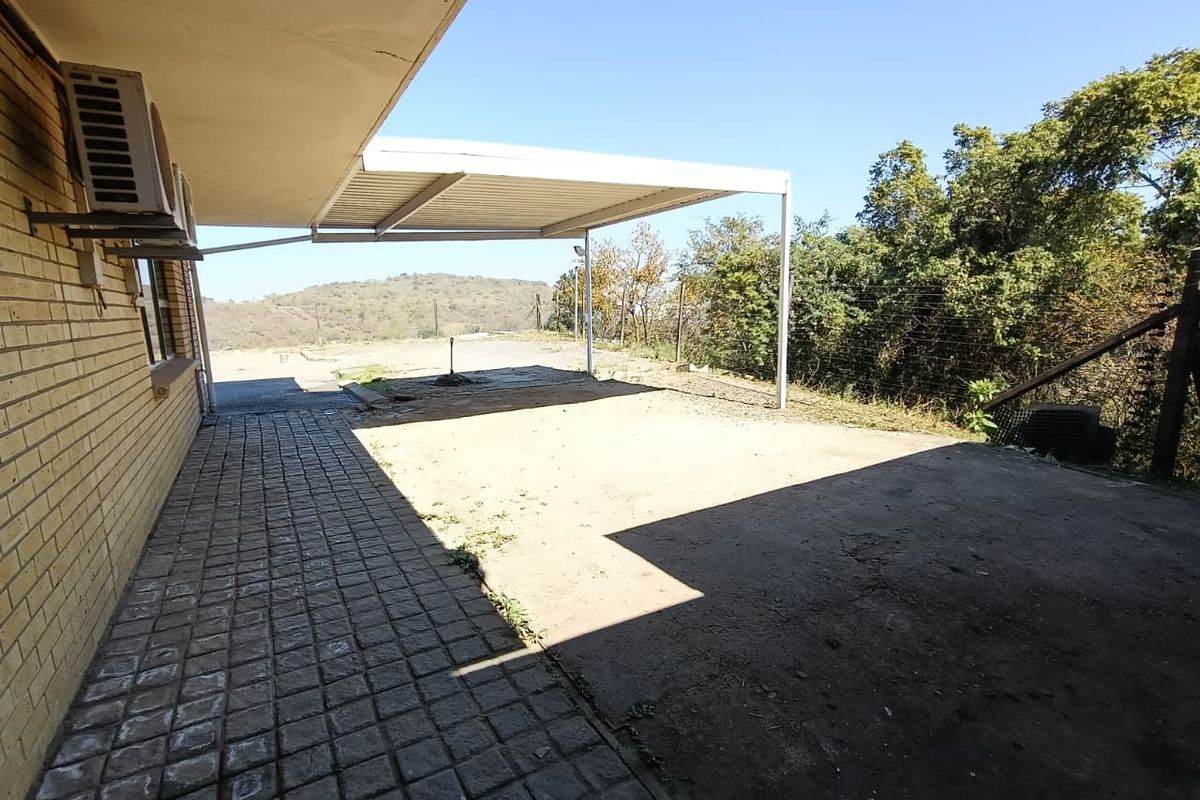 Rear exterior area featuring a brick facade, paved walkway, and a metal carport structure overlooking a natural landscape.