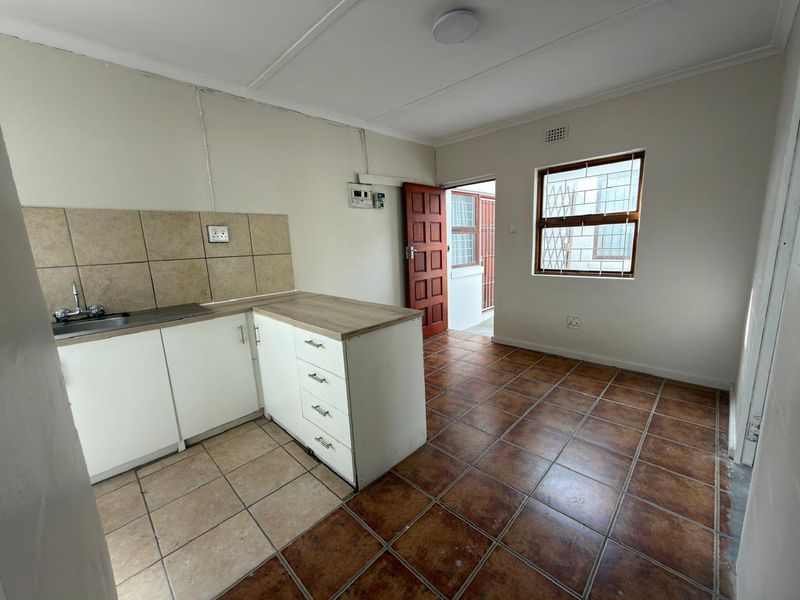 A functional, empty kitchen featuring tiled flooring, basic cabinetry with laminate countertops, a tiled backsplash, and direct access to an exterior security gate.