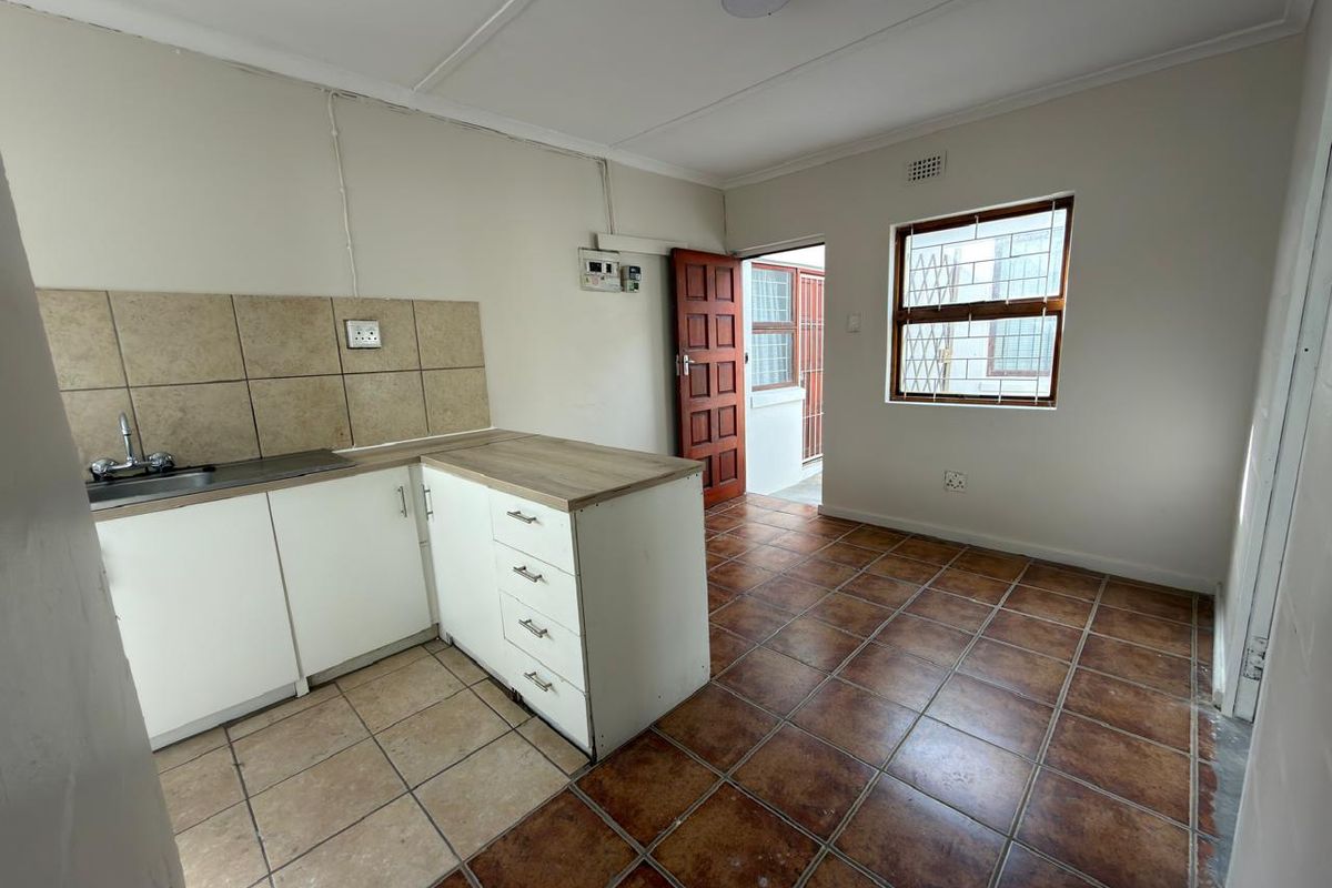A functional, empty kitchen featuring tiled flooring, basic cabinetry with laminate countertops, a tiled backsplash, and direct access to an exterior security gate.