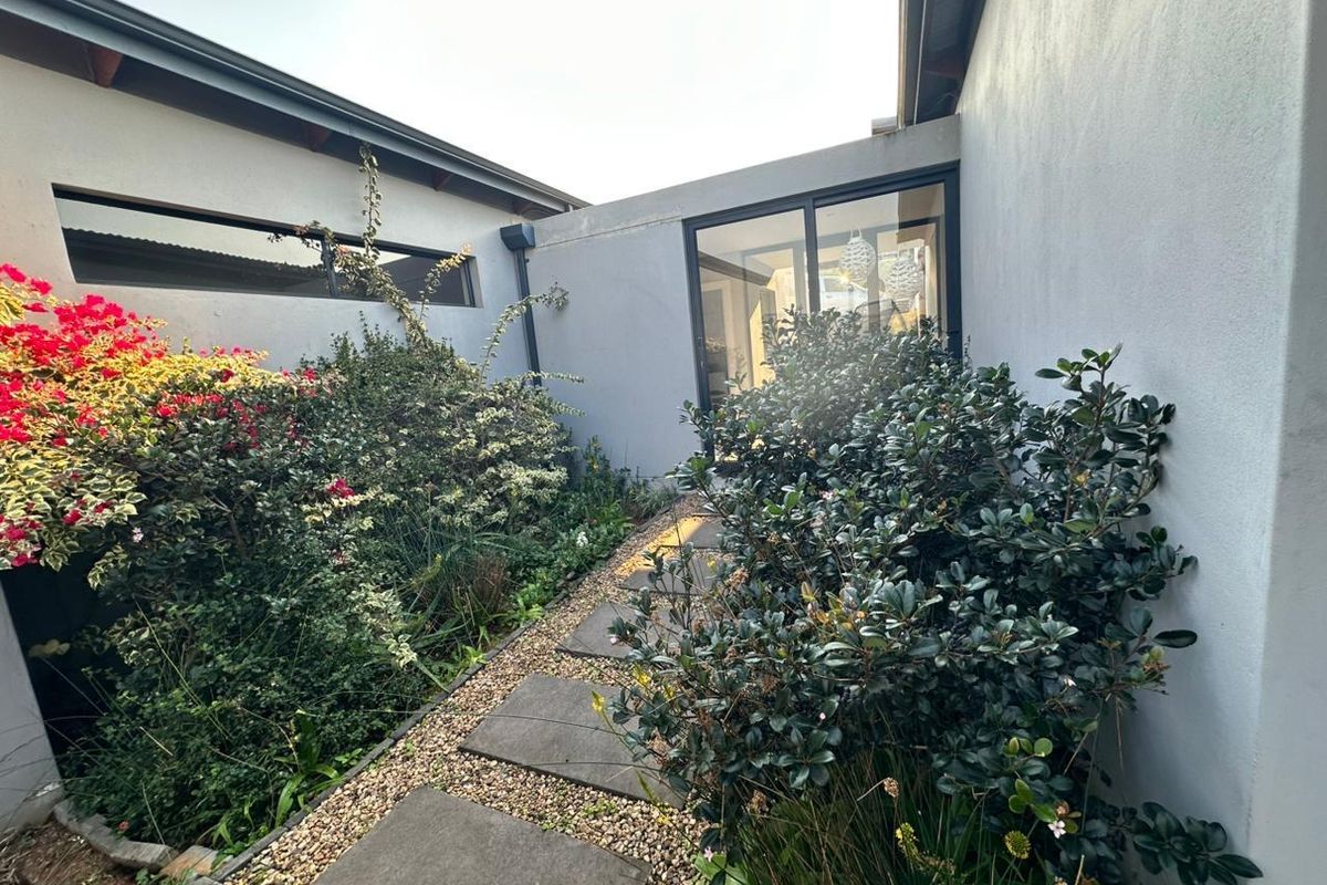 A private rear courtyard featuring a paved walkway, established garden beds, and a large sliding glass door providing access to the home's interior.