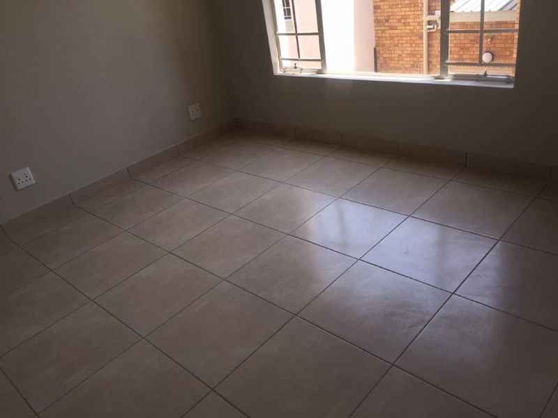 An empty bedroom featuring neutral tiled flooring, tiled skirting, and a window with security bars.