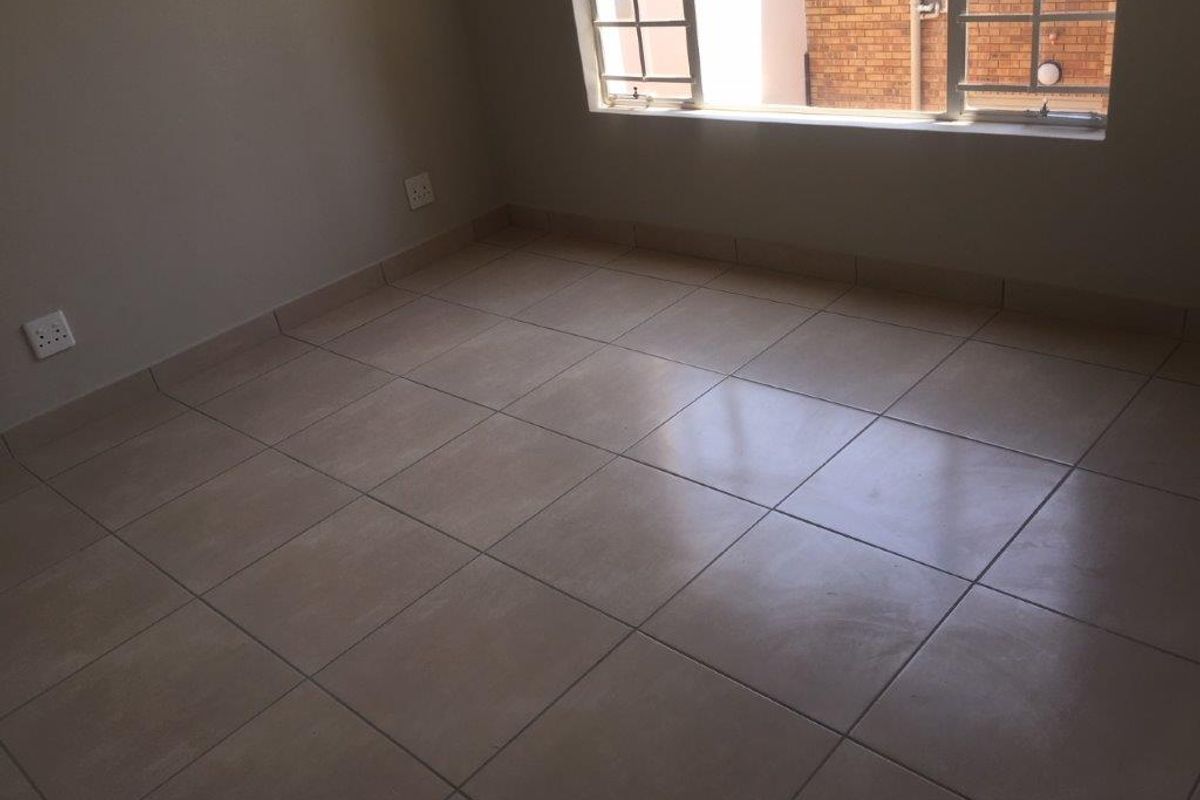An empty bedroom featuring neutral tiled flooring, tiled skirting, and a window with security bars.