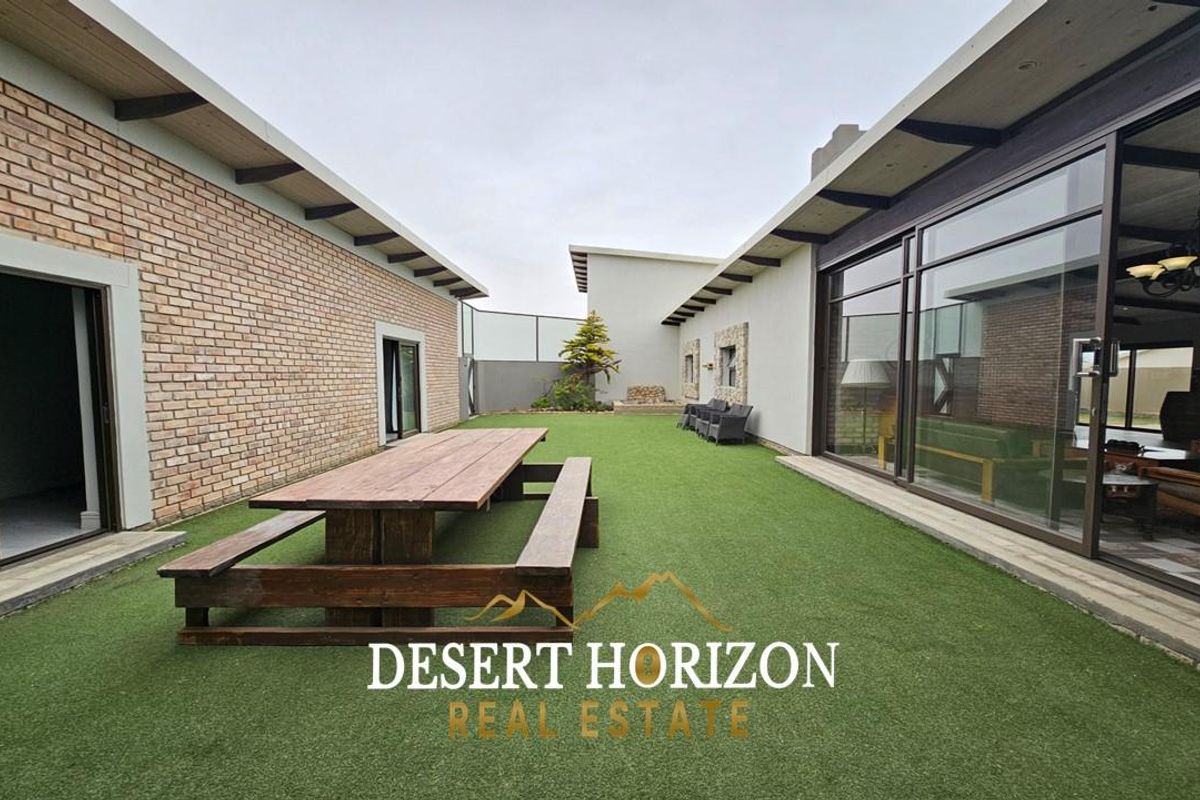 A spacious outdoor courtyard featuring artificial turf, brick wall accents, and large sliding glass doors connecting to the interior living spaces.