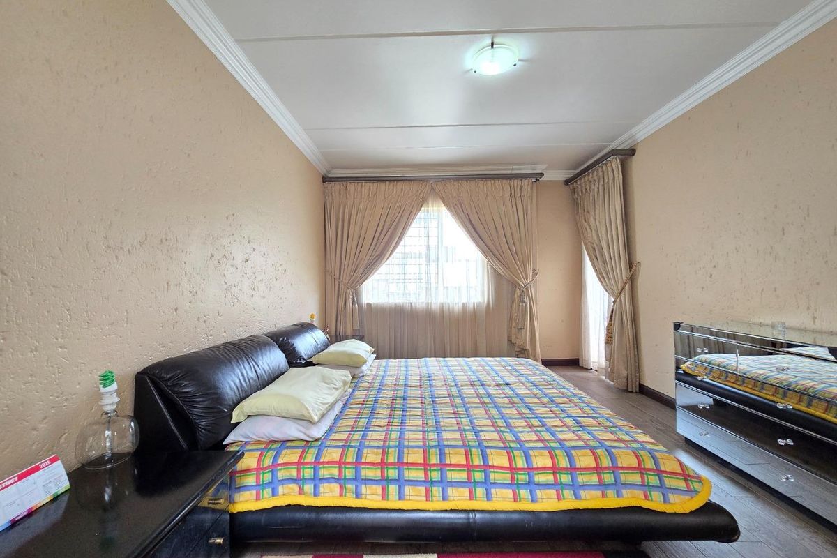 A spacious bedroom featuring wood-look flooring, crown molding, and large windows with curtain tracks, offering a comfortable and functional living space.