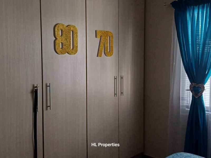 A bedroom featuring light wood-finish built-in cupboards and a window with curtains.