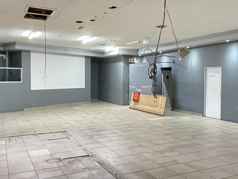 A large, vacant industrial open-plan space featuring tiled flooring, recessed lighting, and exposed electrical infrastructure, requiring significant maintenance and finishing.