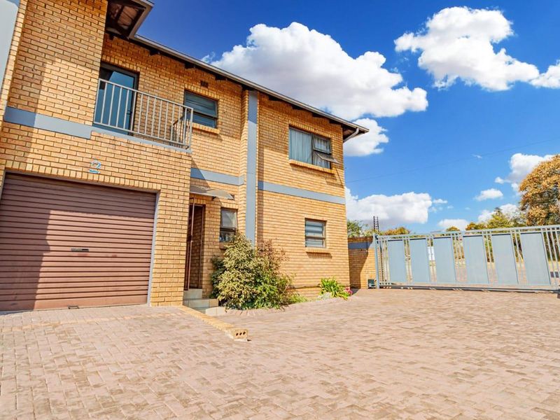 Front exterior view of a facebrick townhouse featuring a single garage, paved driveway, and a balcony with metal railings.