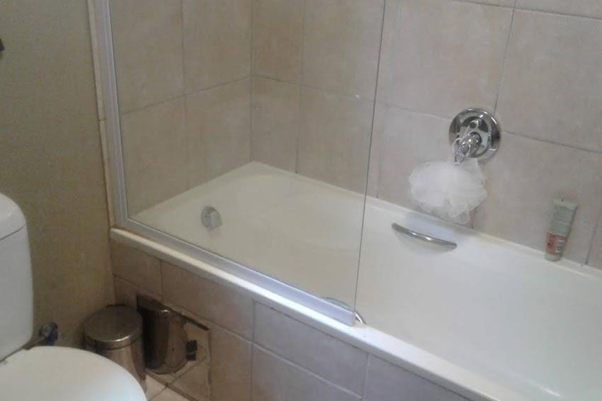 A functional bathroom featuring a bathtub with a glass shower screen, wall-mounted mixer tap, and tiled surround.