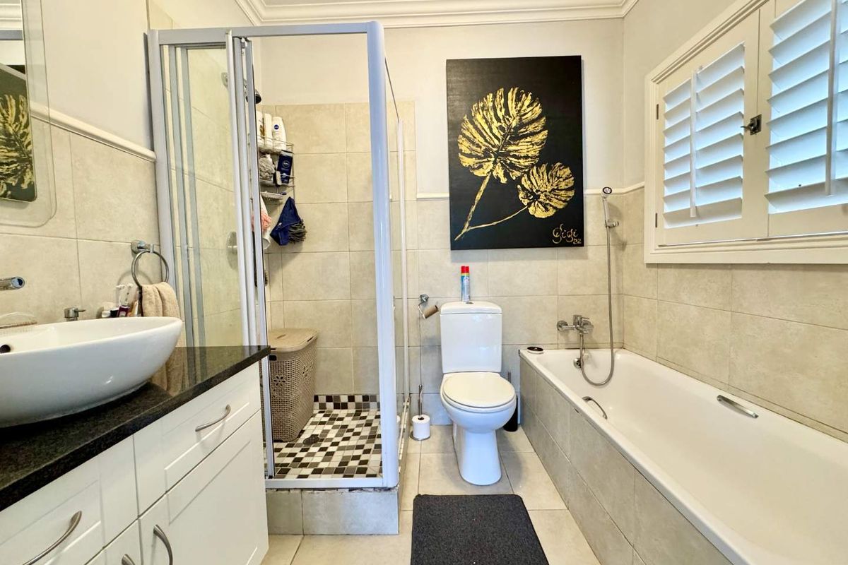 A well-appointed bathroom featuring a separate shower enclosure, a bathtub, a vanity with a vessel sink, and plantation shutters for privacy.