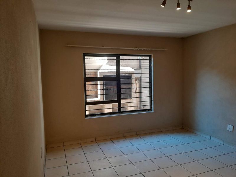 An empty bedroom featuring tiled flooring, a window with security bars, and a ceiling-mounted light fixture, ready for personalization.
