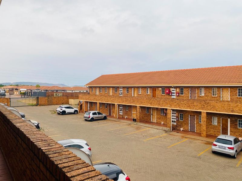 Exterior view of a multi-story face brick apartment complex featuring a paved parking area and secure access points.