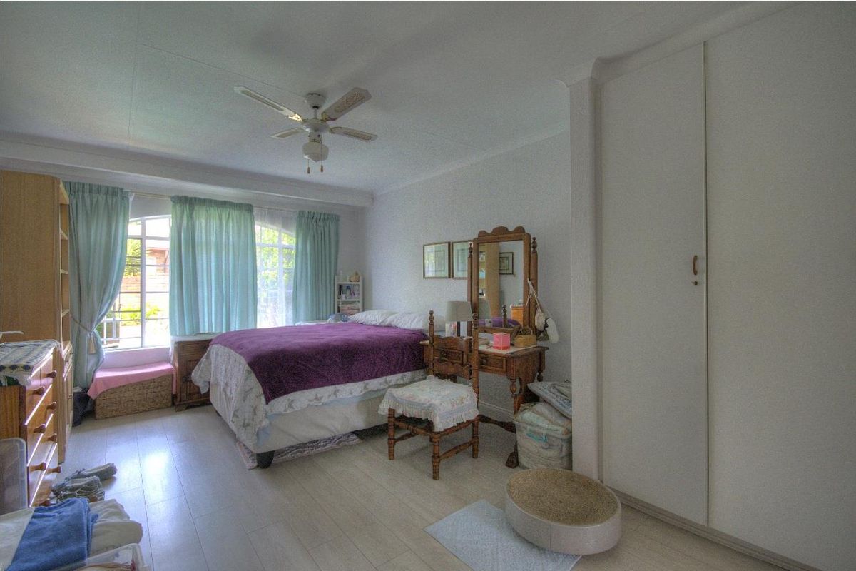 A bedroom featuring built-in cupboards, a ceiling fan, and large windows allowing natural light.