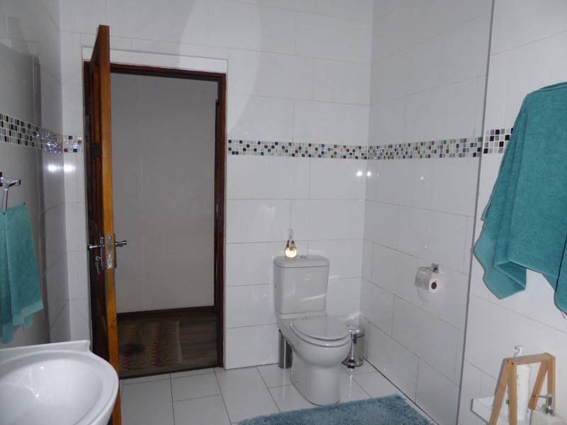 A functional bathroom featuring white wall and floor tiles with a decorative mosaic border, equipped with a standard toilet and pedestal basin.