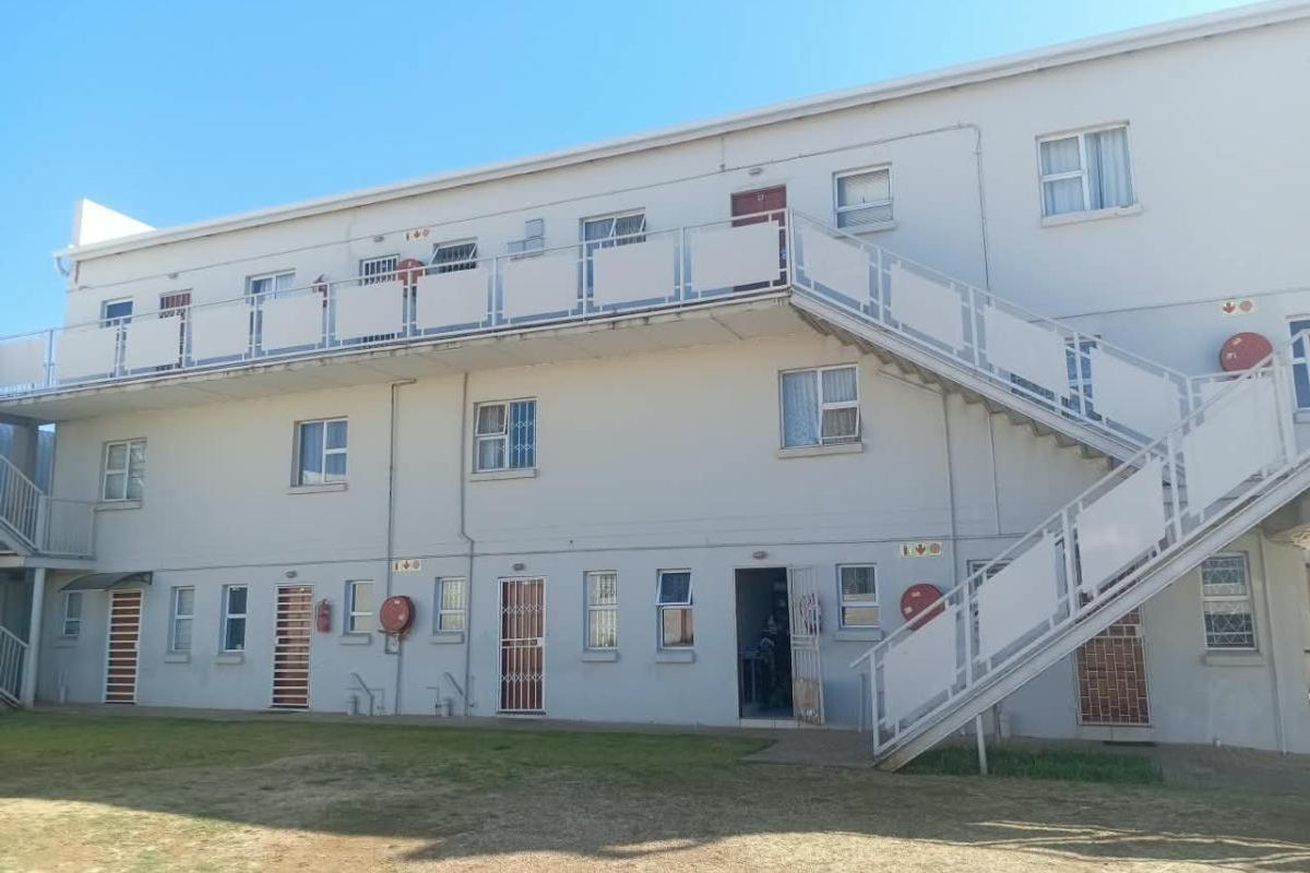 Exterior view of a multi-story apartment block featuring an external staircase, security gates, and metal balustrades.