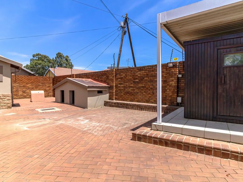 A paved rear courtyard featuring a covered patio area, brick boundary walls with electric fencing, and stone-clad exterior wall details.