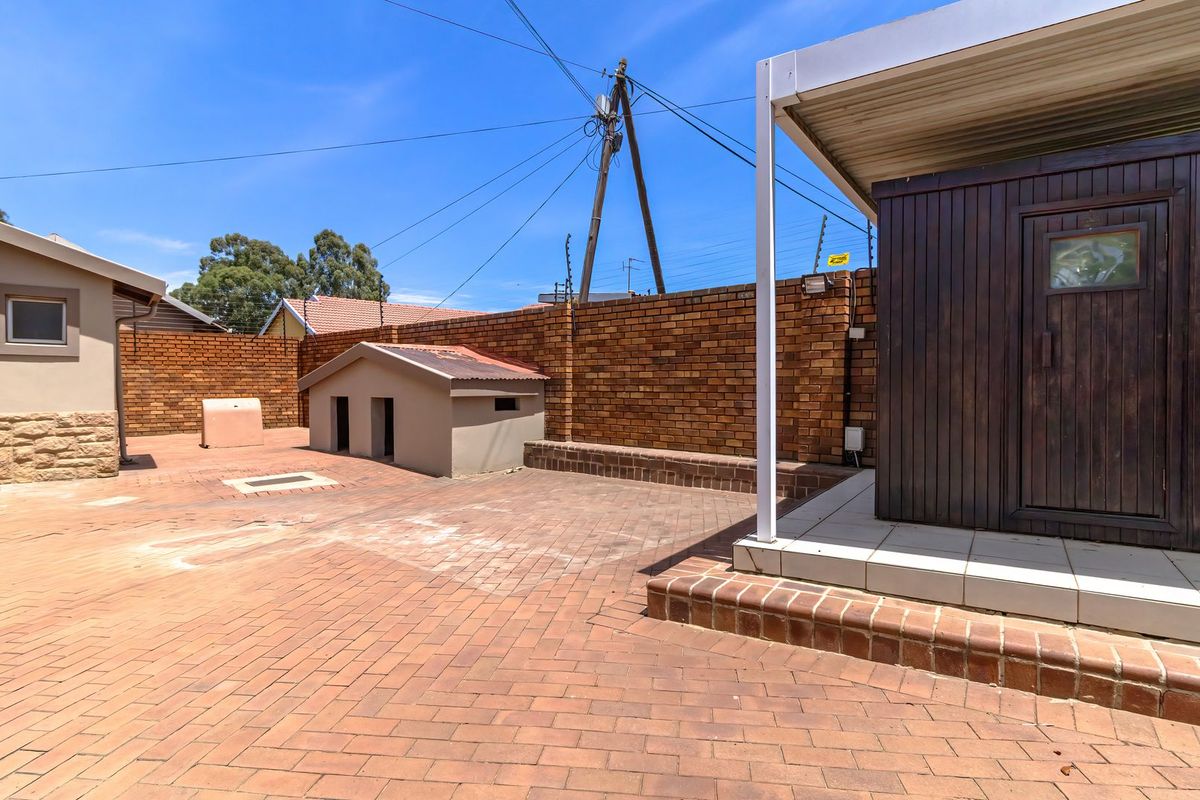 A paved rear courtyard featuring a covered patio area, brick boundary walls with electric fencing, and stone-clad exterior wall details.