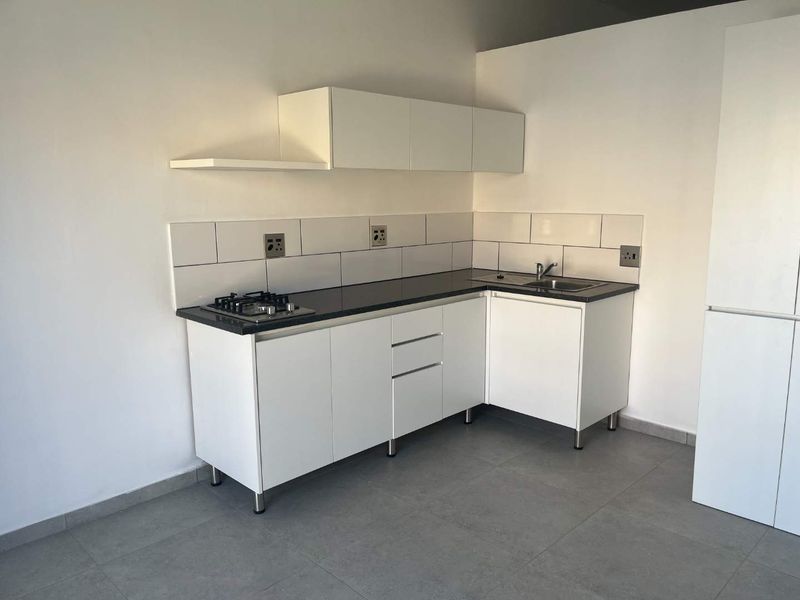 A clean, modern kitchen featuring white cabinetry, a dark stone countertop, a built-in gas hob, and a stainless steel sink with a tiled backsplash.