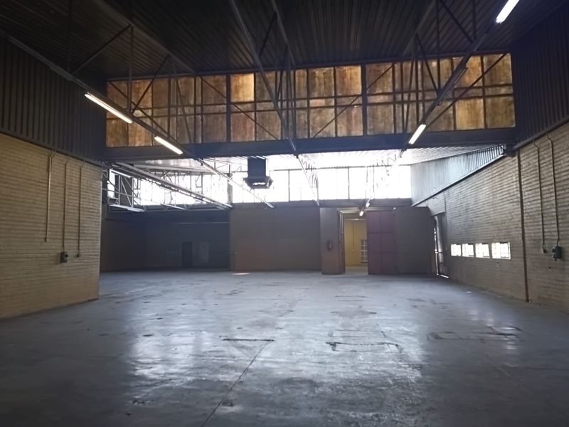A large, open-plan industrial office space featuring high ceilings with exposed steel trusses, concrete flooring, and ample natural light from clerestory windows.