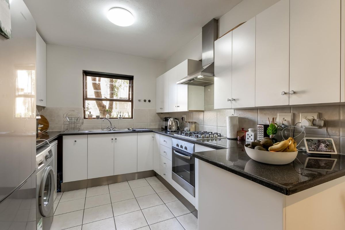 A functional kitchen featuring white cabinetry, granite countertops, a gas hob, stainless steel oven, and integrated laundry facilities.