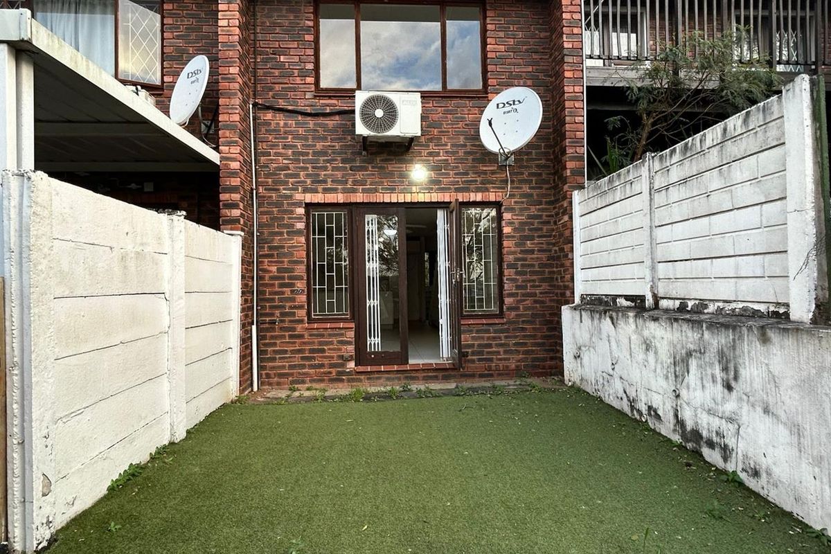 Rear view of the townhouse featuring a private courtyard with artificial turf, brick facade, and direct access through glass-paneled doors.