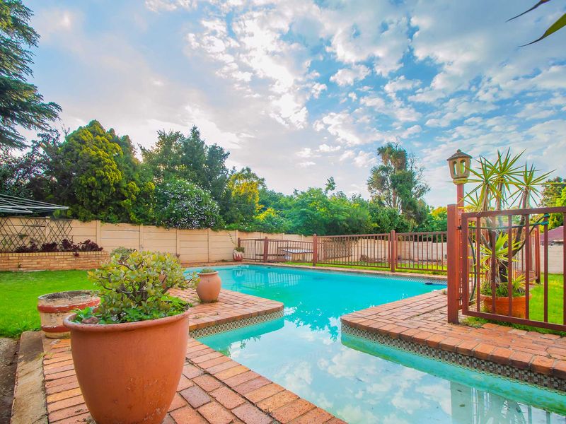 Outdoor pool area featuring a swimming pool with brick coping, enclosed by metal fencing and a precast concrete boundary wall.