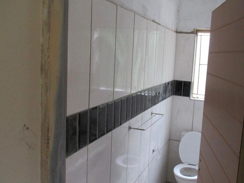 A small bathroom featuring tiled walls with a decorative border, a toilet, and a window with security bars, currently in an unfinished state.