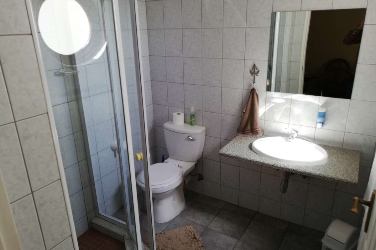 A functional bathroom featuring a glass-enclosed shower, a wall-mounted vanity with a basin, and a standard toilet, finished with neutral wall and floor tiling.