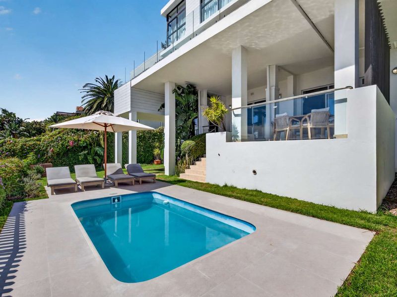 A well-maintained outdoor pool area featuring a modern swimming pool, concrete decking, and a covered patio with glass balustrades.