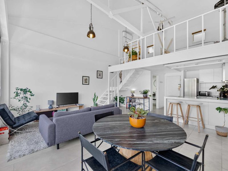 Spacious open-plan apartment featuring a mezzanine level, exposed roof trusses, modern kitchen cabinetry, and a breakfast counter, creating a bright and airy living space.