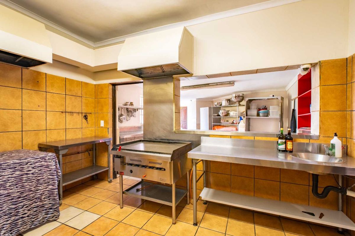 Commercial-style kitchen featuring stainless steel prep surfaces, a built-in griddle, extractor hood, and tiled finishes, suitable for high-volume food preparation.