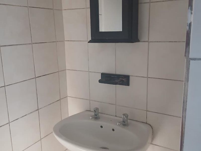 A compact bathroom featuring a pedestal basin, wall-mounted medicine cabinet, and tiled walls, requiring cosmetic updates to improve its overall condition.