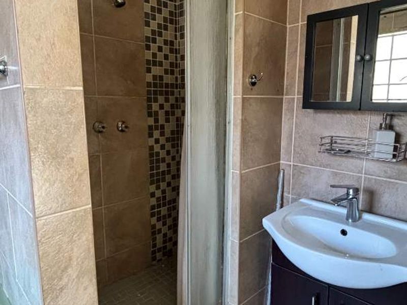 A functional bathroom featuring a shower enclosure, vanity cabinet with basin, and tiled finishes throughout.