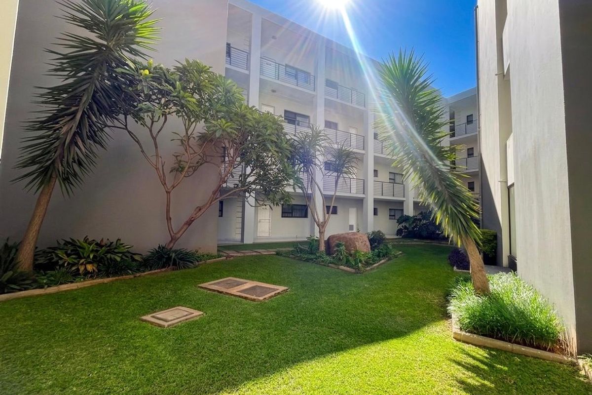 A well-maintained communal garden area situated between apartment building blocks, featuring landscaped lawns and established trees.