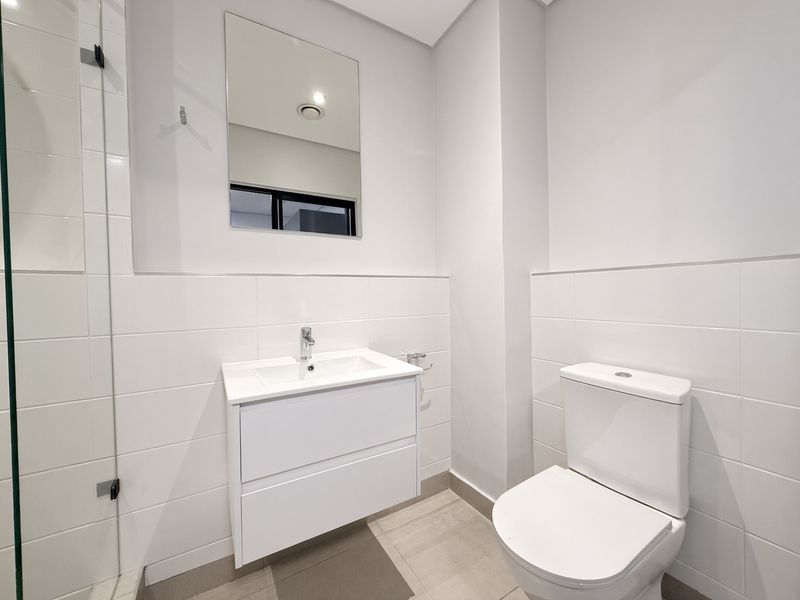 A modern, clean-lined bathroom featuring a wall-mounted vanity, dual-flush toilet, and a glass-enclosed shower with neutral tiled finishes.