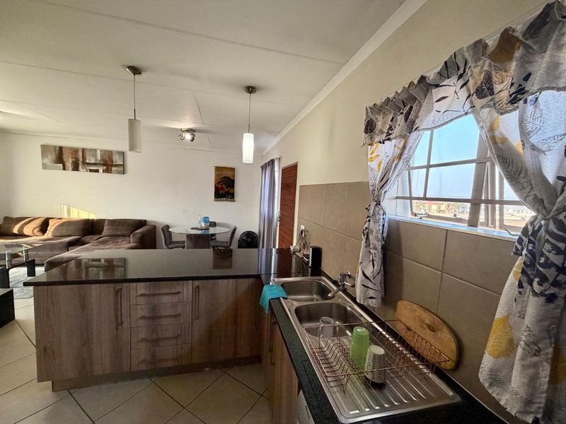 Open plan kitchen and living area featuring granite countertops, double sink, laminate cabinetry, and tiled flooring in a well-maintained apartment setting.