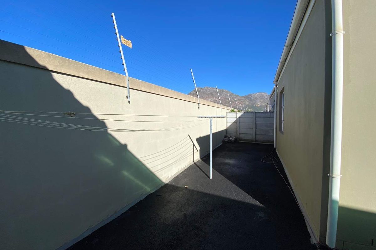 A side exterior area of the townhouse featuring a paved walkway, boundary wall with electric fencing, and a downpipe.