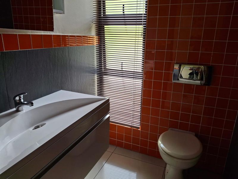 Modern bathroom featuring a wall-mounted vanity with basin, wall-hung toilet with concealed cistern, and vibrant orange tiled wall accents.